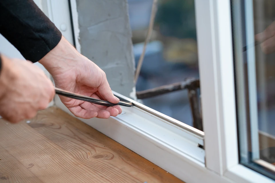 Intérieur résidentiel, personne installant un joint d'étanchéité sur châssis de fenêtre à l'aide d'une pince à sertir