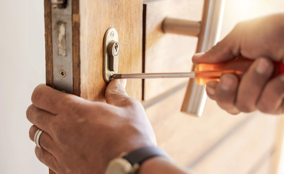 Intérieur résidentiel, mains d'une personne utilisant un tournevis pour démonter ou réparer une serrure de porte en bois